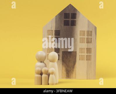 Holzhaus und Miniaturfiguren einer Familie auf gelbem Hintergrund. Das Konzept des Verkaufs und Kaufs von Immobilien, Investitionen Stockfoto