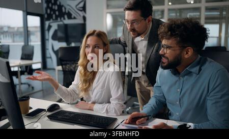Drei gestresste, problembeladene multikulturelle Bürokollegen, die auf den Laptop schauen, reden, streiten, ein Problem diskutieren, Misserfolg, Online-Arbeit, Vielfalt Stockfoto