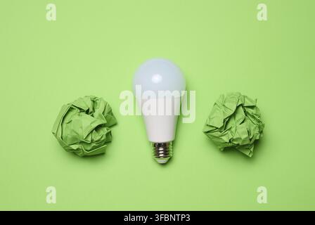 Zerknitterte grüne Papierkugeln und weiße Glaslampe auf grünem Hintergrund, Draufsicht Stockfoto