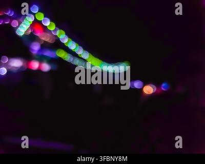 Abstrakter Bokeh-Hintergrund aus farbenfrohen Lichtern in der Nacht. Unscharf leuchtende runde Formen in Lila, Grün und Rosa, isoliert auf einem dunklen Hintergrund. Stockfoto