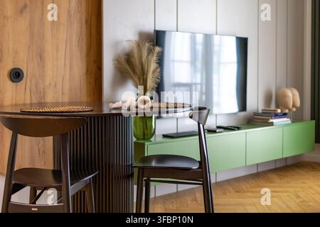 Essbereich mit Tisch und Stühlen öffnet sich zu einem gemütlichen Wohnzimmer mit Fernseher in einer modernen Wohnung. Konzept von Open-Space-Innenarchitektur und Komfort Stockfoto