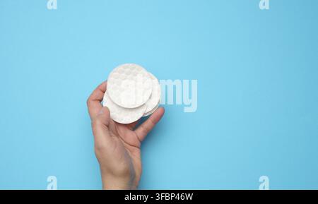 Weibliche Hand hält saubere runde weiße Baumwolle Make-up-Entferner Pads auf blauem Hintergrund Stockfoto