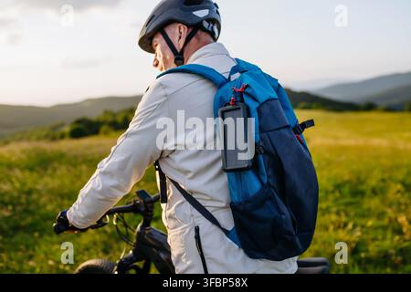 Senior-Radtourist nutzt einen tragbaren Solarladegerät, um sein Smartphone im Freien mit Strom zu versorgen. Stockfoto