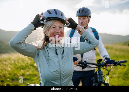 Aktives älteres Paar bereitet sich auf eine Radtour vor und setzt Helm auf. Stockfoto