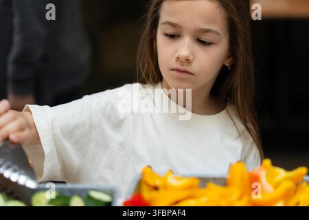 Vorpubertäres Mädchen wählt frisches Gemüse von einem Buffet in einem modernen Hotelrestaurant aus und entscheidet sich während des Frühstücksservices für gesundes Essen Stockfoto