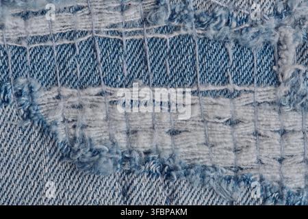 Detailliertes Makro-Bild von zerrissenem blauem Denim mit freiliegenden weißen Fäden und grober Webart Stockfoto