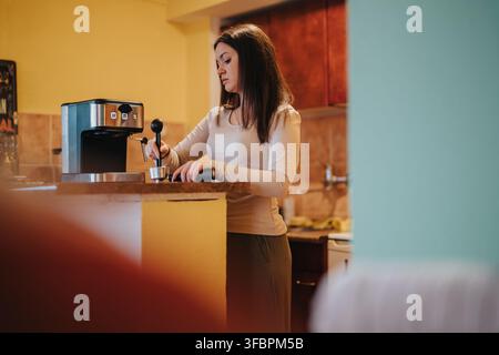 Junge Frau macht Espresso-Kaffee an der Küchentheke zu Hause mit einer modernen Espressomaschine Stockfoto