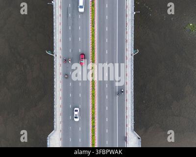 Luftbild aus der Top-Down-Perspektive einer Brücke über einem Fluss mit Autos und Motorrädern, die über Fahrspuren fahren, die durch einen grünen Mittelstreifen mit roten Bordsteinen getrennt sind Stockfoto