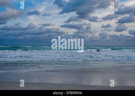 Wellen krachen am Ufer unter bewölktem Himmel in der Dämmerung an einem Strand. Stockfoto