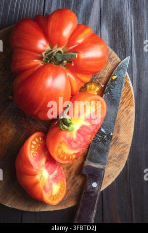 Ganze und geschnittene Heirloom-Tomaten auf Holzbrett mit Messer. Rustikale Küchenszene, Biohof-Produkte Stockfoto