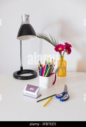 Zurück-zur-Schule-Konzept – Stifte, Kugelschreiber, Scheren, Locher, Radiergummi, Lampe und eine Vase mit Blumen. Stockfoto