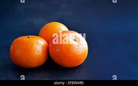 Hohe Blickwinkelaufnahme von reifen Bio-Mandarinens. Lebendige orangefarbene Früchte auf schwarzer Textur. Minimalistische Komposition perfekt für Food-Marketing, Gesundheits-Banner Stockfoto