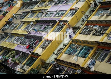 Eine diagonale Niederwinkelaufnahme fängt die dicht gedrängte, farbenfrohe Fassade eines Hongkonger Mietshauses ein, das abwechselnd gelbe und violette Abschnitte aufweist Stockfoto