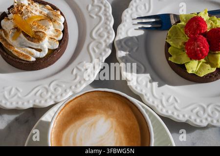 Zwei verschiedene Gourmet-Tarten, die auf weißen Tellern neben einer Tasse Kaffee serviert werden. Stockfoto