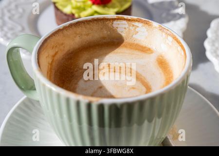 Ein frisch gebrühter Cappuccino mit zarter Blatt-Latte-Art, serviert in einer gerippten hellgrünen Tasse mit Untertasse. Stockfoto