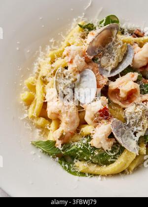 Meeresfrüchte-Pasta-Gericht mit Linguine, Garnelen, Muscheln in cremiger Parmesansauce mit Knoblauch, Kräutern, Basilikum, Tomaten, Grünzeug auf sauberem weißem Teller, frisch Stockfoto