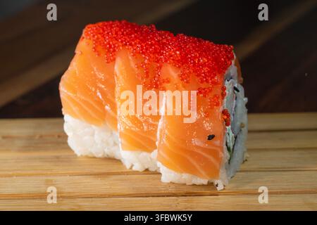 Eine Gourmet-Lachs- und Tobiko-Sushi-Rolle, serviert auf einem Holzbrett. Stockfoto