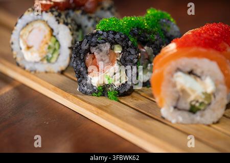 eine bunte Auswahl an köstlichen Sushi-Rollen und Maki, die auf einem Holzbrett arrangiert sind. Stockfoto