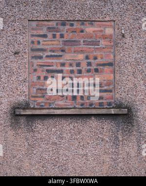 Altes mit Ziegeln gefülltes Fenster an einer strukturierten Kieselputz-Außenwand Stockfoto