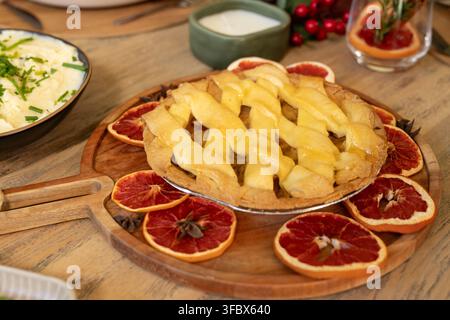 Eine Obstkuchen-Scheibe ruht auf einem hölzernen Servierbrett auf dem Tisch neben Kartoffelpüree und getrockneten Zitrusfrüchten Stockfoto
