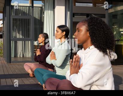 Verschiedene Frauenfreundinnen im Schneidersitz meditierend auf der Terrasse zu Hause mit Yogamatten, Leggings Stockfoto