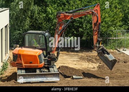Bagger manövriert einen Erdbewegungsanhänger auf einer aktiven Baustelle. Der Bediener ist in der Kabine sichtbar und arbeitet unter klarem Himmel mit Bäumen im Hintergrund. Stockfoto