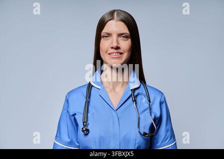 Porträt einer lächelnden Krankenschwester in blauem Kittel mit Stethoskop vor grauem Hintergrund Stockfoto