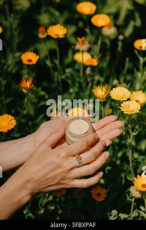 Eine ruhige Nahaufnahme von Händen, die ein Glasgefäß mit lebendigen gelben und grünen Blumenstielen in einem üppigen Blumenfeld halten, das eine beruhigende und nat Stockfoto