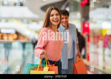 Zufriedene junge Frau lächelt und hält bunte Einkaufstüten, Einkaufszentrum Stockfoto