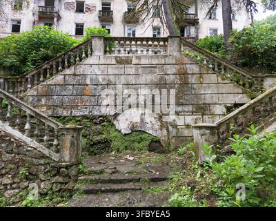 Verlassene Steintreppe, die in der Stadt Akarmara, Abchasien, mit grüner Vegetation überwuchert ist. Grandios symmetrische Stufen eines verfallenen Gebäudes, bedeckt mit Moos. Stockfoto