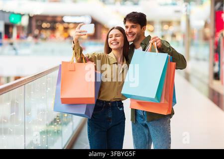 Glückliches junges Paar macht Selfie beim gemeinsamen Einkaufen in einer modernen Mall Stockfoto