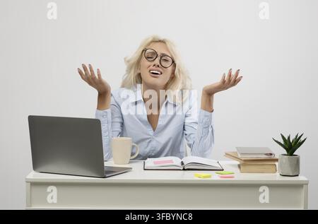 Frustrierte blonde Frau mit Brille sitzt am Schreibtisch im Büro, Geschäftskonzept Stockfoto