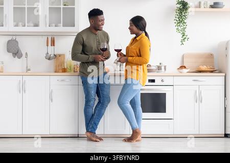 Glückliches schwarzes Paar genießt Gläser Wein in einer modernen Küche, romantischer Abend zu zweit Stockfoto