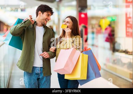 Glückliches junges Paar beim Einkaufen in der Mall, trägt bunte Taschen, Einzelhandelskonzept Stockfoto