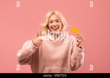 Zufriedene junge Frau hält gelbe Karte und zeigt Daumen hoch, positives Lebensstil-Konzept Stockfoto