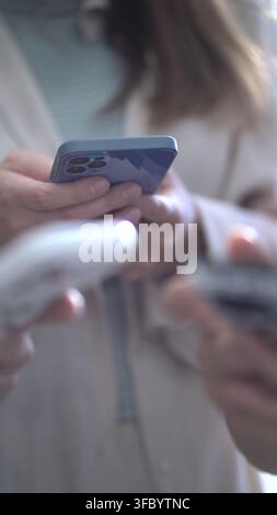 Frauen in lässiger Kleidung, die nebeneinander Smartphones verwenden, Nahaufnahme von Händen, die weiße und gemusterte Hüllen halten, zeitgenössischer Lebensstil und digital Stockfoto