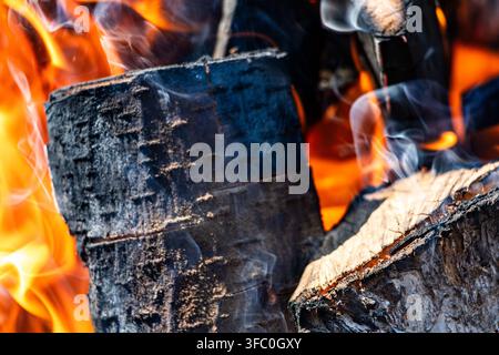 Nahaufnahme eines verkohlten Holzscheits in einem heißen Lagerfeuer mit aufsteigendem Rauch im Freien, niemand im Bild. Stockfoto