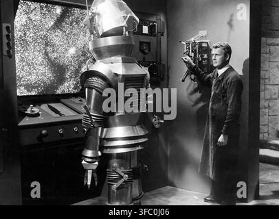 Ein Schwarz-Weiß-Publicity-Still aus dem Science-Fiction-Film "Tobor the Great" von 1954 mit dem Schauspieler Charles Drake als Dr. Ralph Harrison, der mit dem großen, metallischen Roboter Tobor interagiert. Der Roboter ist mit einem durchsichtigen Kuppelkopf und einer komplexen Greifhand dargestellt und steht neben einem Bildschirm, auf dem ein sternenklarer oder pixeliger kosmischer Bildschirminhalt zu sehen ist. Stockfoto