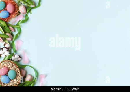 Frohe Ostern. Bunte Eier, Tulpen, ein Baumwollzweig auf blauem Hintergrund. Flat Lay Grußkarte Kopierraum Stockfoto