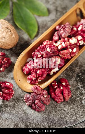 Rote Walnusskerne in einer hölzernen Schöpfkelle auf einer grauen Steinfläche. Stockfoto