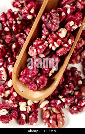 Nahaufnahme von roten Walnusskernen in einer Holzschaufel auf weißem Hintergrund. Stockfoto