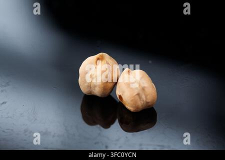 Zwei getrocknete Kichererbsen auf einer dunklen reflektierenden Oberfläche in einer Studio-Umgebung. Stockfoto