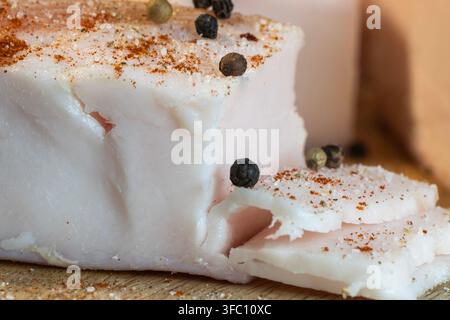 Eine Nahaufnahme zeigt dicke Stücke rohen, gewürzten Schweinefetts oder Salo, die mit schwarzen Pfefferkörnern, Salz und Paprika belegt sind. Stockfoto