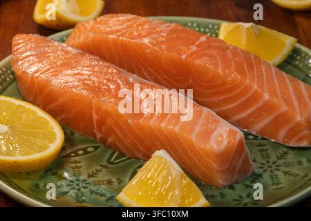 Frische rohe Lachsfilets, garniert mit Zitronenscheiben, sind auf einem Teller arrangiert. Stockfoto