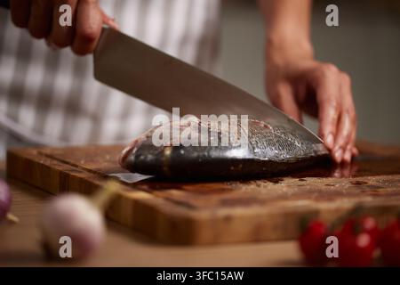 Chef-Hände bereiten frischen Salzwasserfisch auf einem Holzschneidebrett in einer Küche vor. Lebensmittelzubereitung mit Meeresfrüchten Stockfoto