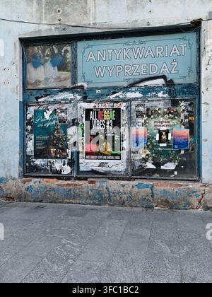 Eine Nahaufnahme eines alten Schaufensters in £ódŸ, Polen, mit abblätternder blauer Farbe, freigelegtem Ziegelstein und mehreren Konzert- und Werbepostern. Der Stockfoto