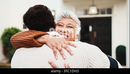 Senior, glückliche Frau und Sohn an der Haustür mit Umarmung, Willkommen zu Hause und Trost bei sicherer Rückkehr. Verbindung, aufgeregte Mutter oder Umarmung Mann im Freien für Stockfoto