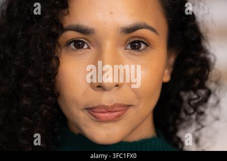Afroamerikanerin schaut in die Kamera im Studio und zeigt einen dunkelgrünen gerippten Pullover und lockiges Haar. Porträt, Kopfshot, gelassen, warm, Nahaufnahme, Bokeh Stockfoto