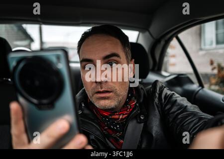 Ein junger Fahrer, der sich vor dem Lenkrad von seinem Telefon abgelenkt hat und sein Smartphone während der Fahrt mit einer Hand benutzte. Risiko- und Gefahrensituation Stockfoto