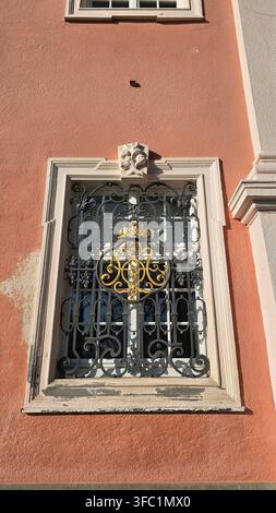 Uhldingen-Muhlhofen, Deutschland - 28. Dezember 2025. Detail eines Fensters mit vergoldetem schmiedeeisernem Gitter an der rosa Fassade des Klosters Birnau. Stockfoto
